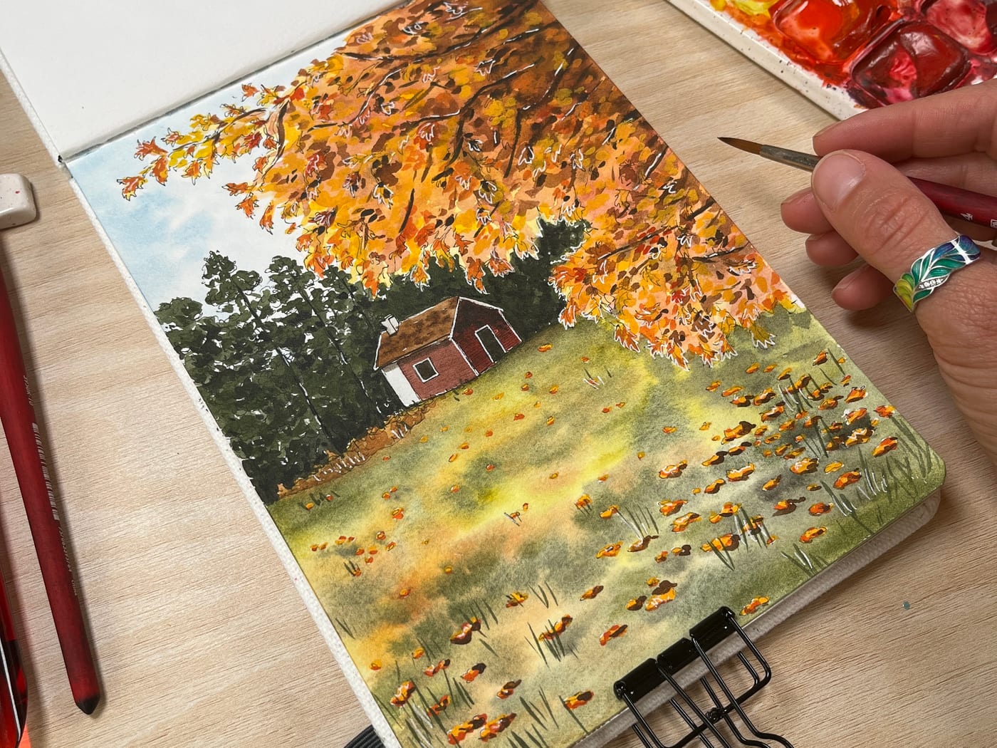 Watercolour landscape of a red cottage under an autumn tree beside a meadow