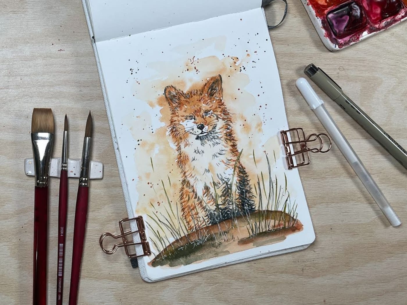 Watercolour painting of a young fox sitting in the grass