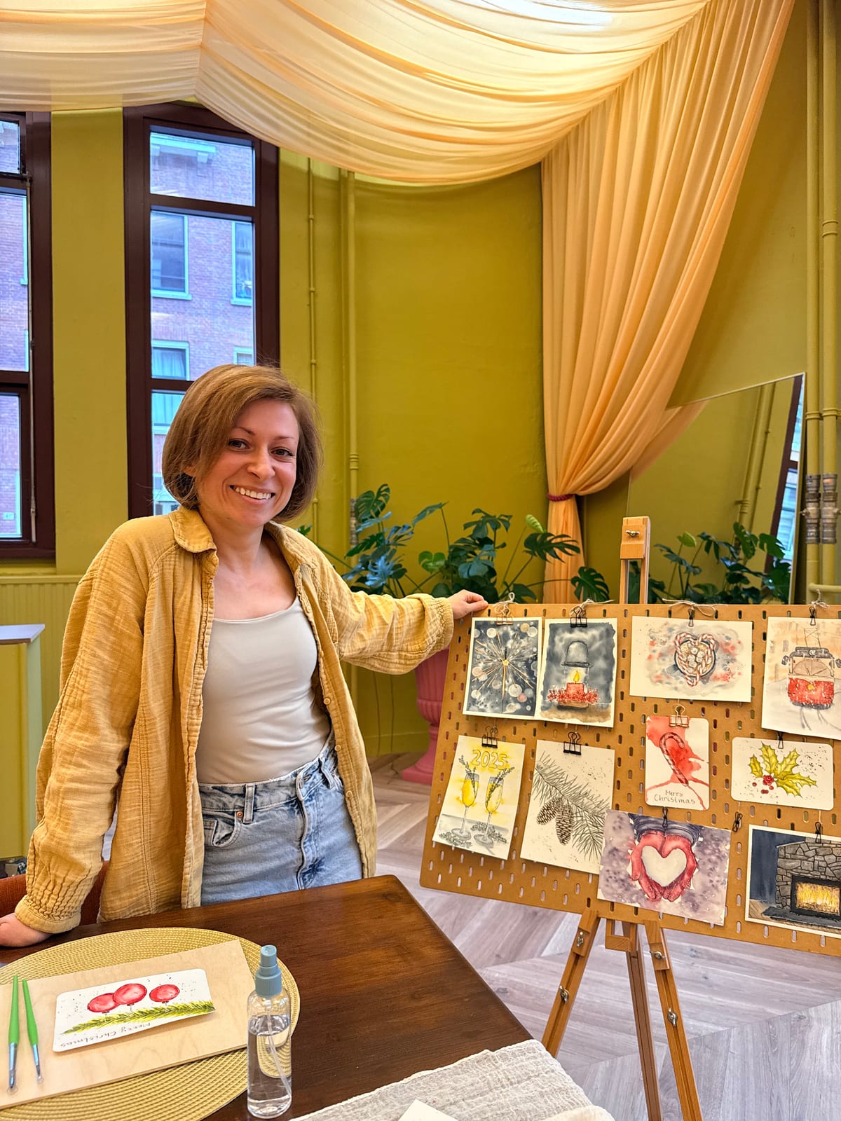 Gabriela smiling beside an easel hung with ink and watercolour Christmas cards