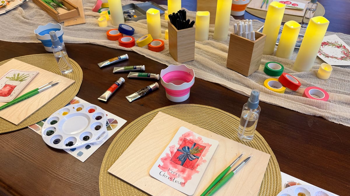 A table set for a Christmas card workshop with candles, paints, brushes and washi tape