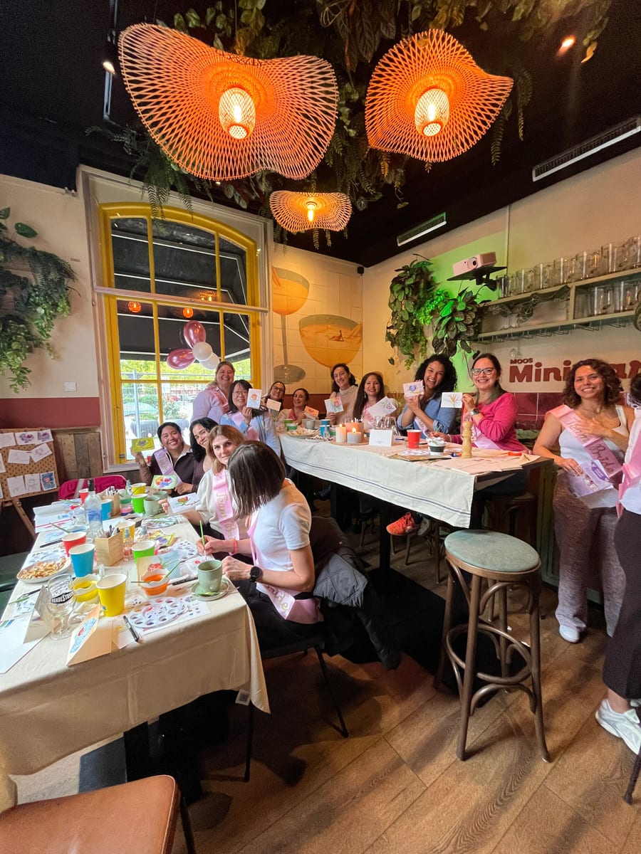 The whole room mid workshop, balloons at the window and everyone holding up their paintings